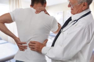 Male Doctor and patient suffering from back pain during medical exam after car accident injury