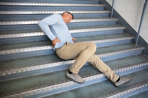 A man clutching his lower back, sprawled on steps capped with galvanized metal; personal injuries from slip and fall accidents can cause long-lasting pain and suffering.