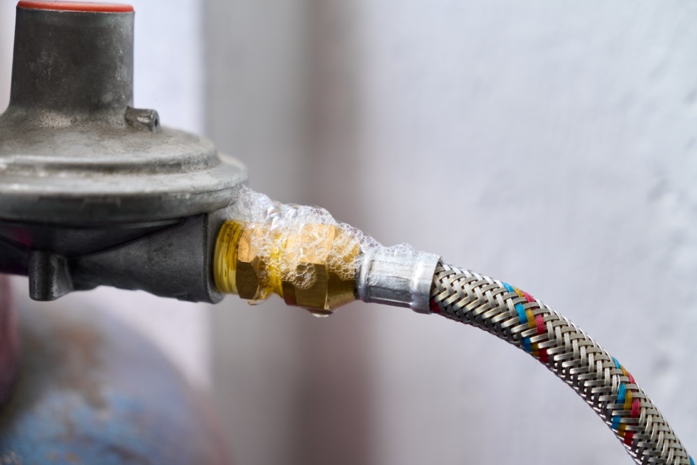 Soap bubbles forming around a brass fitting where a braided gas hose connects to a regulator, showing a gas leak