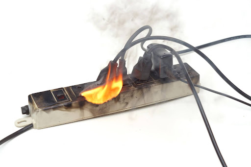 Surge protector on fire, with smoking appliance cords attached; a product liability lawyer handles cases arising from defective product malfunctions.