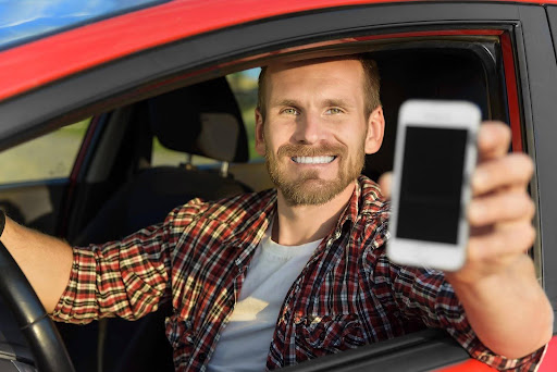 An Uber driver in his car, holding out his phone. Suing uber may be a complicated process, so it is important to understand the details of how an Uber lawsuit works.