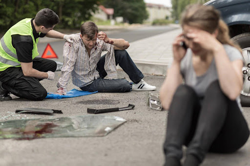Two drivers sitting in the road at the scene of a car accident; one is being attended by a paramedic while the other speaks on a mobile phone. What happens at the crash site can influence whether you need to go to court for a car accident.