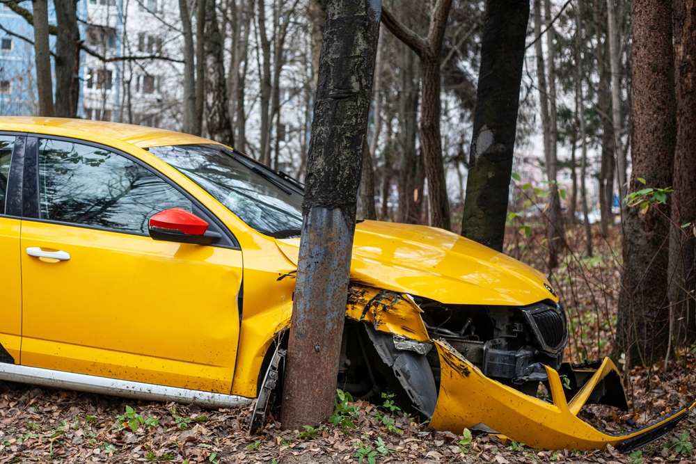 Yellow car with severe front-end damage after crashing into a tree, illustrating the risk of a serious car accident