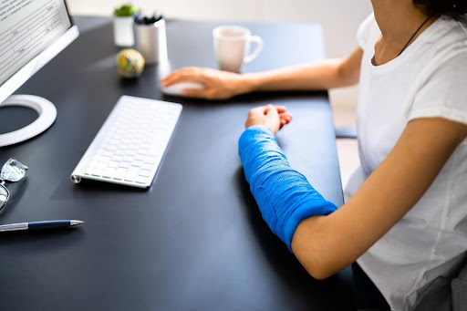 A woman with a blue arm cast filing online forms to settle out of court after a slip and fall injury.