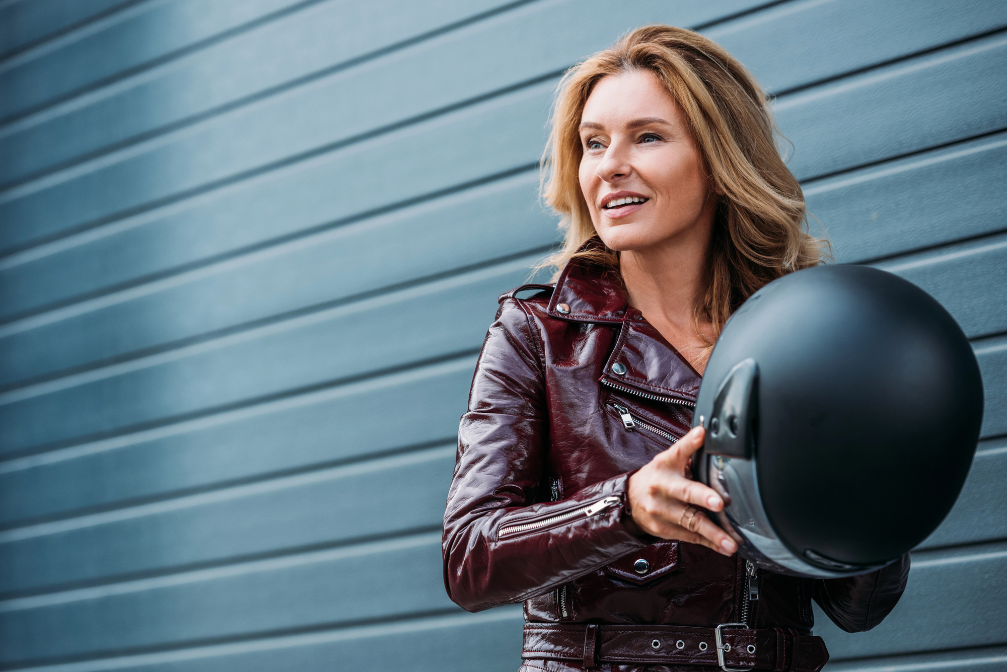 A woman in a leather jacket holds a motorcycle helmet to wear, complying with motorcycle helmet laws.