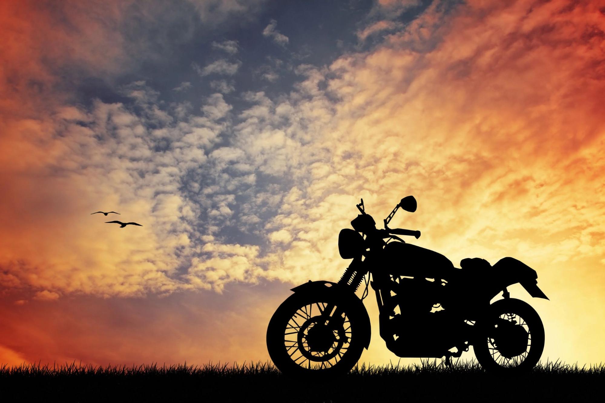 The silhouette of a motorcycle sits in a field with a sunset in the background; a class M motorcycle license may be required in Pennsylvania to ride a motorbike.