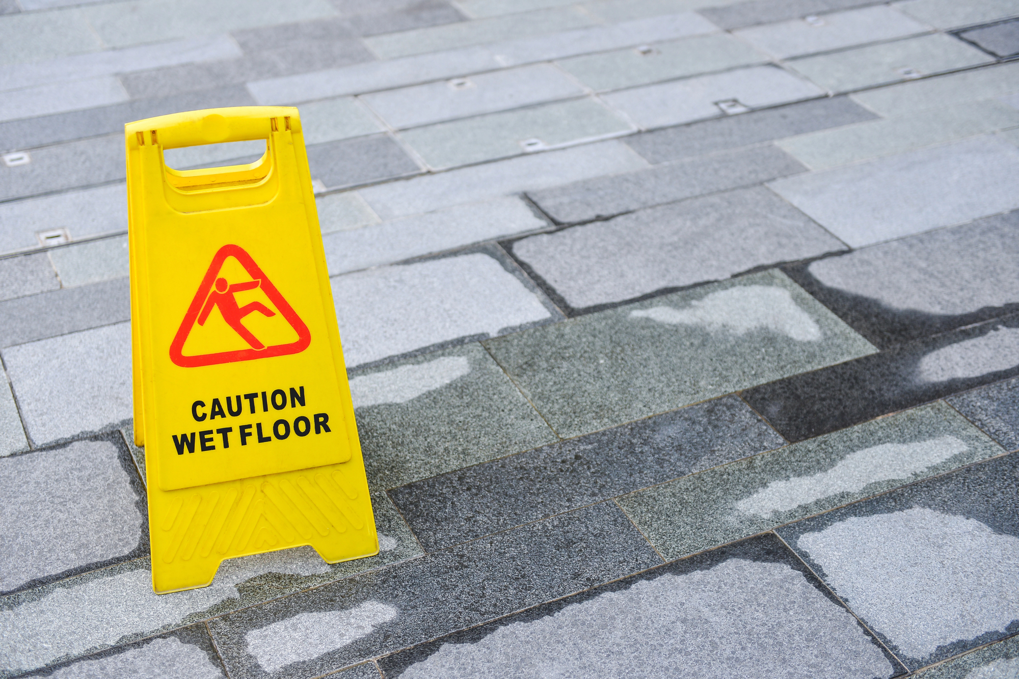 Yellow caution wet floor sign on a tiled surface with visible water, illustrating a common slip and fall hazard in fall accident cases.