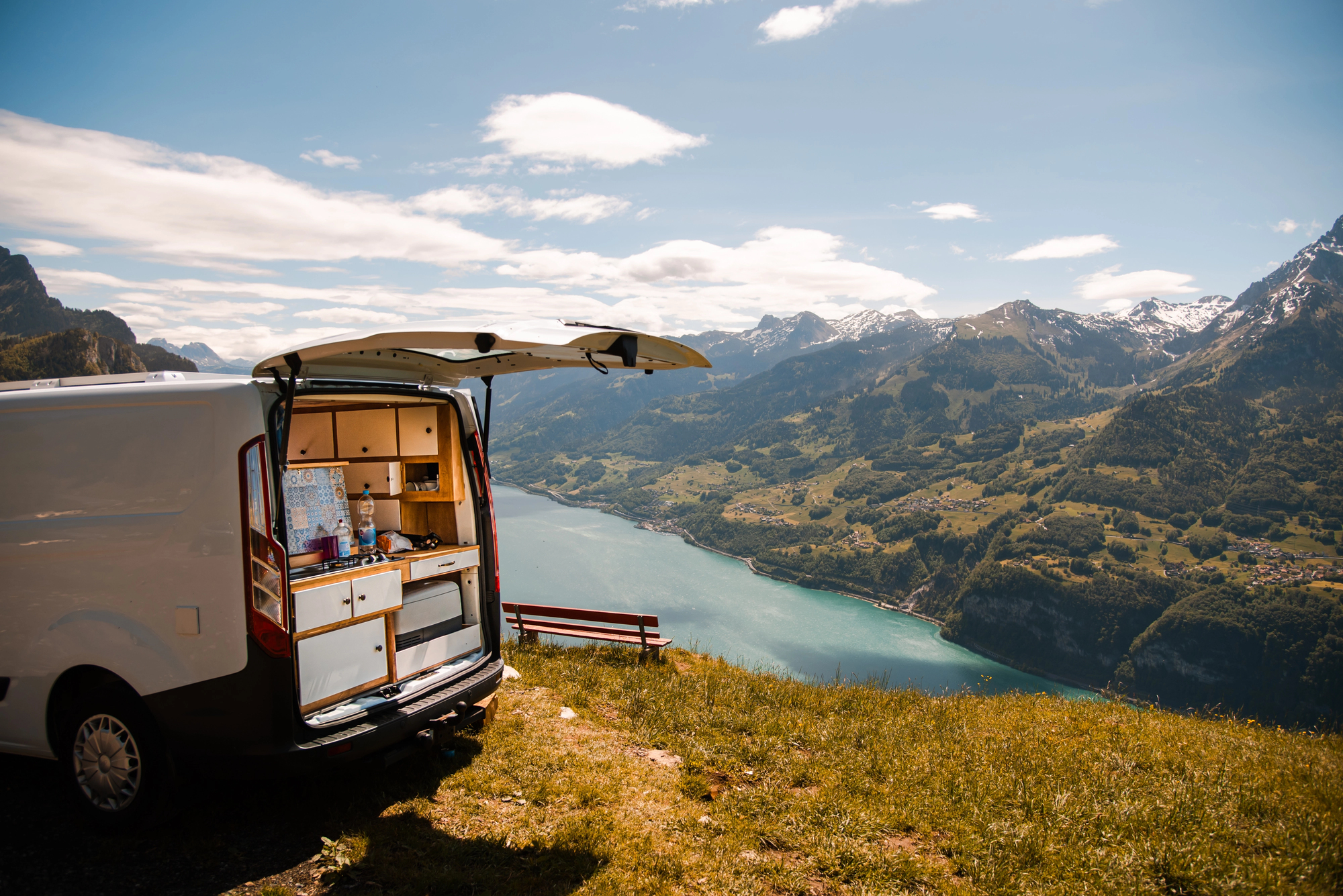 Rear image of a van outfitted as a temporary residence, set against a mountain background; conversion vans can provide exciting travel opportunities but also pose risks.