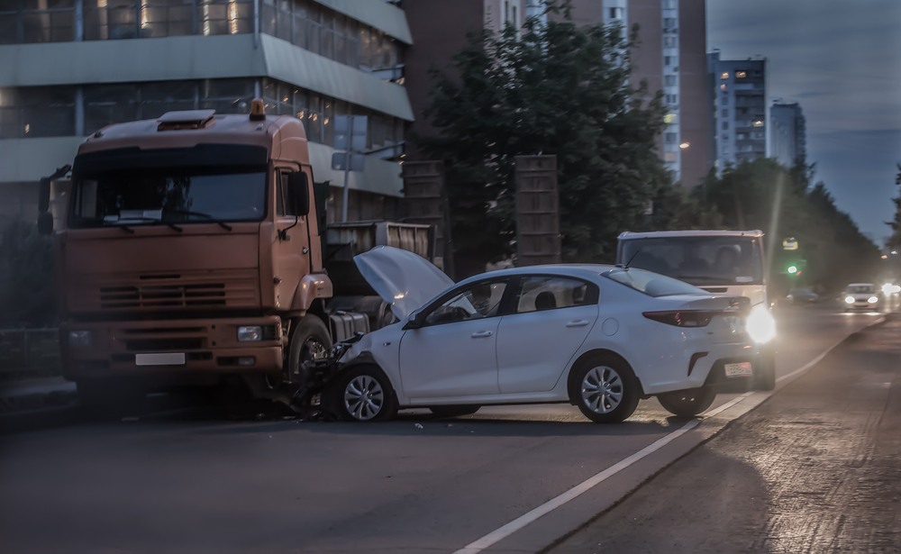 White sedan with front-end damage after colliding with a truck at night on a city street