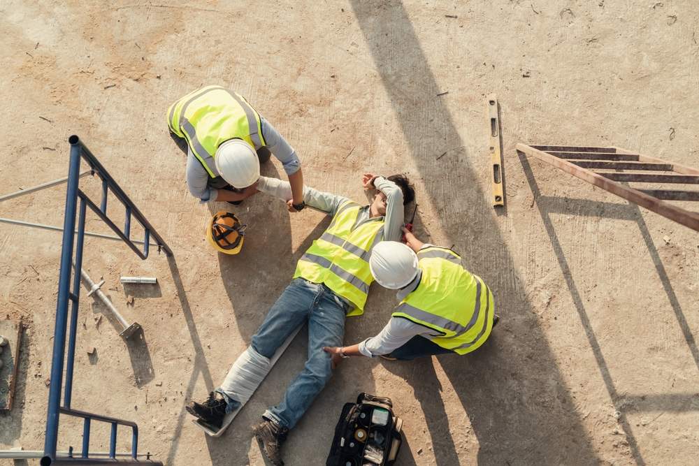 Aerial view of two coworkers helping an injured worker lying on the ground at a construction site