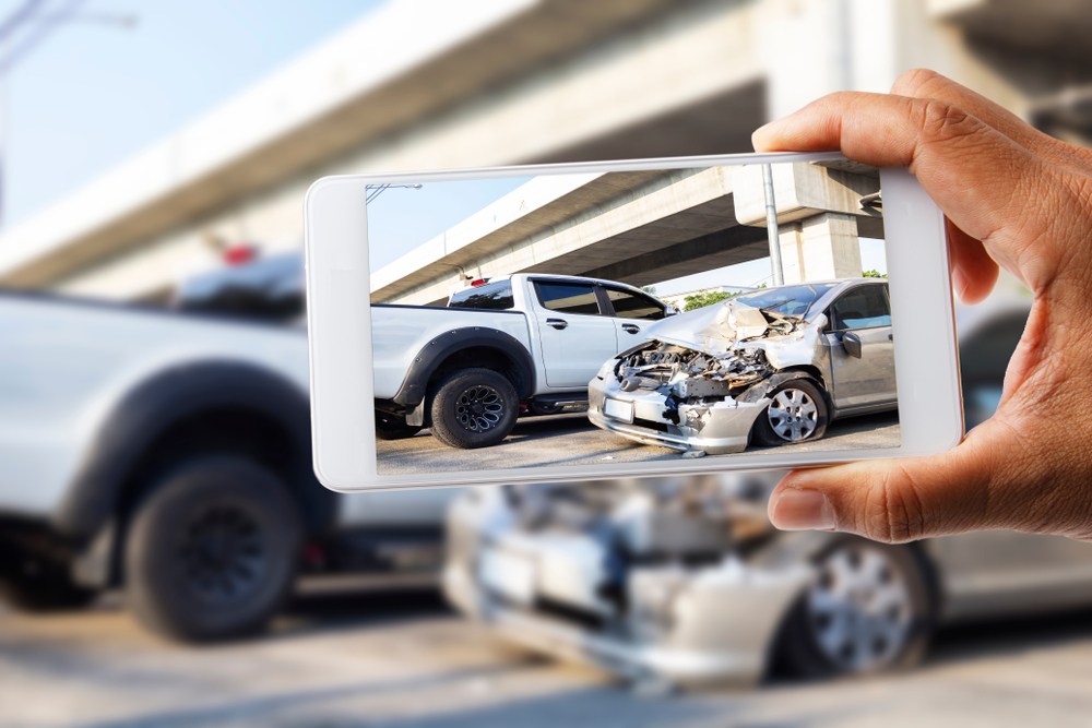 Person photographing a car accident scene with a smartphone to document vehicle damage