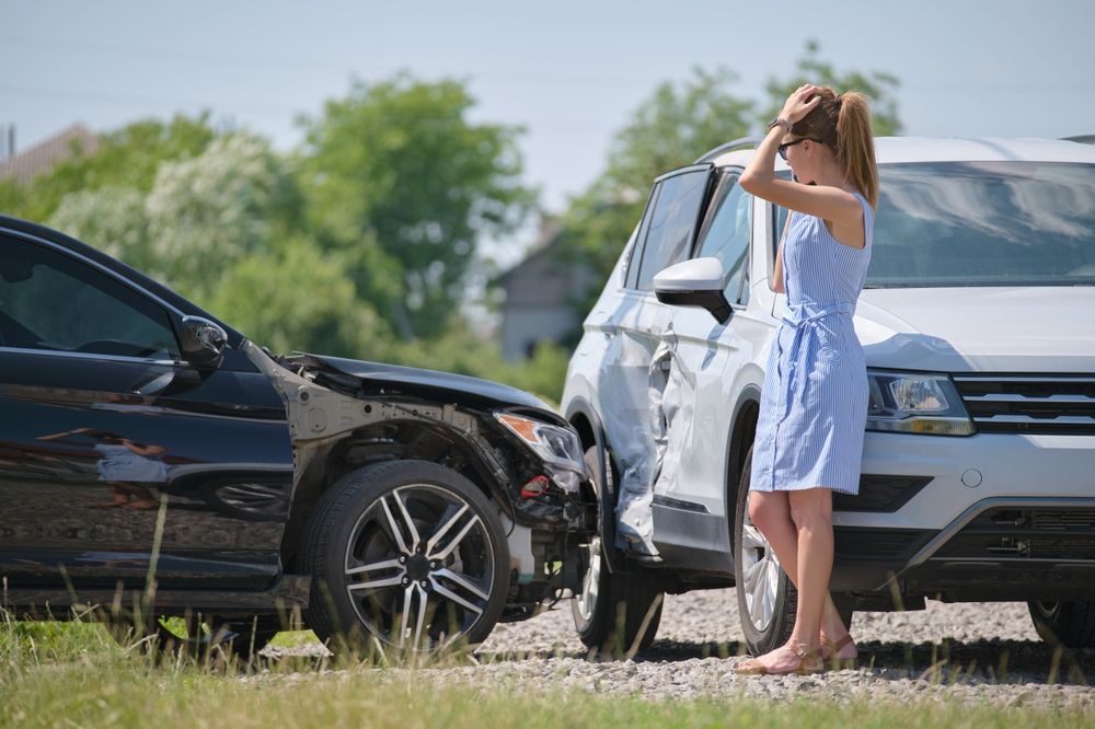 Woman holding her head in distress standing between two crashed vehicles