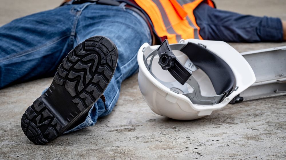 Construction worker lying on the ground with a fallen hard hat beside a ladder after a workplace accident