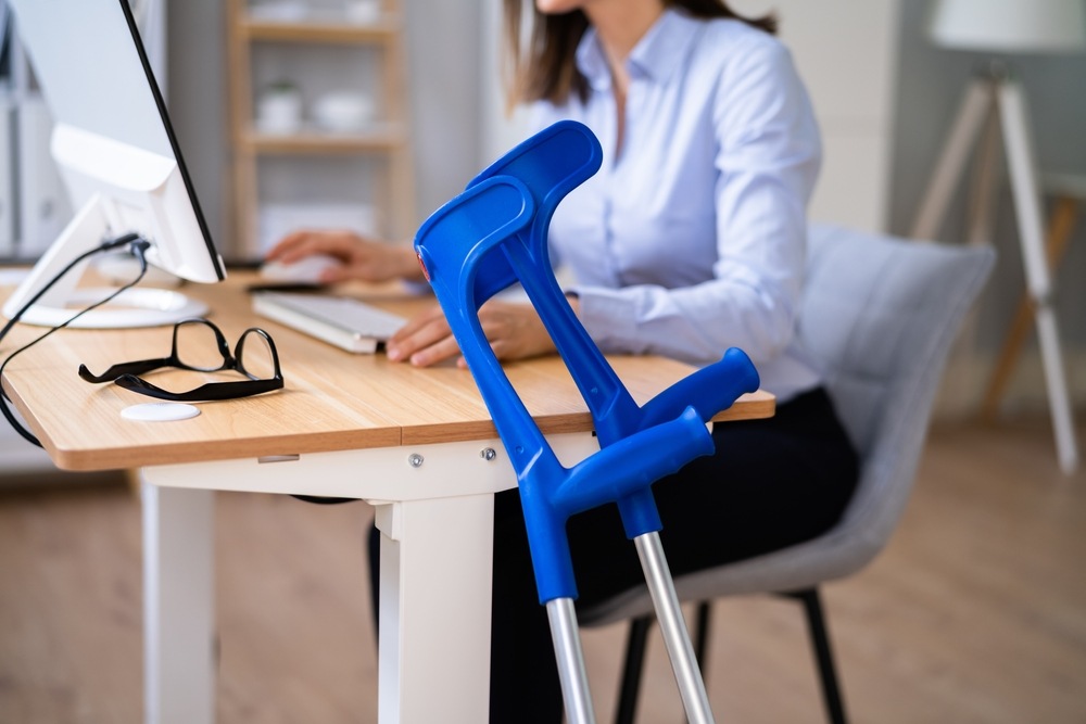 Crutches leaning against a desk beside an office worker, representing a workplace injury recovery in Philadelphia