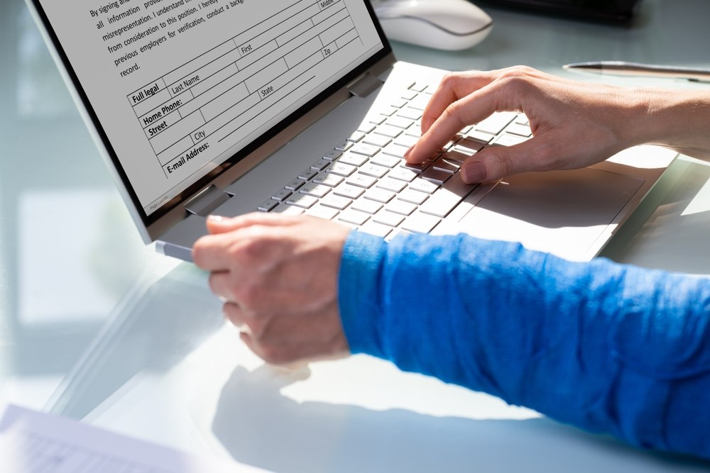 Person with an arm cast typing a workers' compensation claim form on a laptop