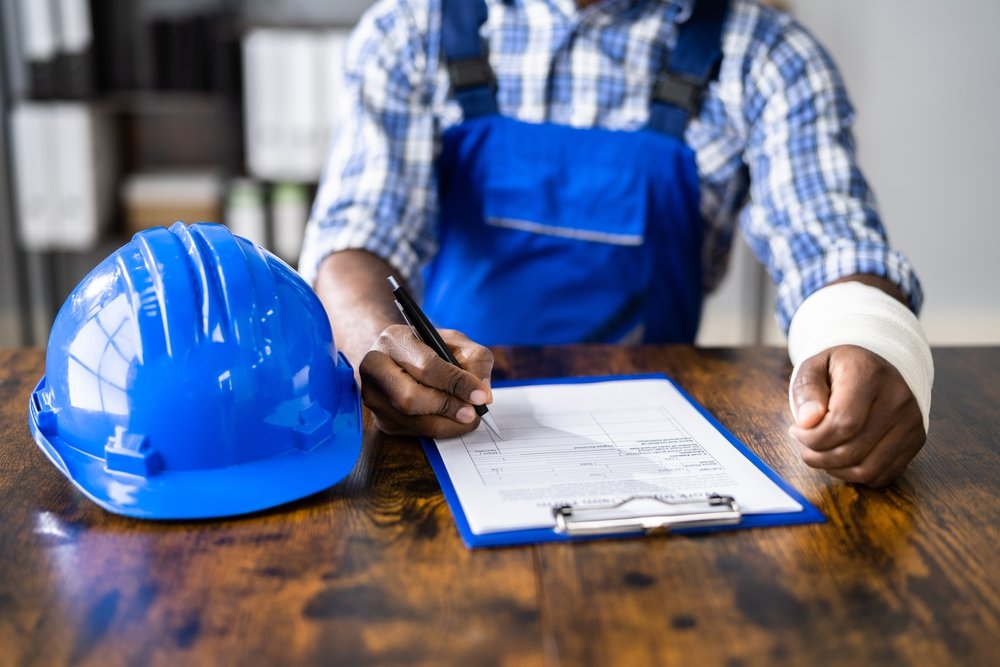 Construction worker in Philadelphia with a bandaged wrist filling out a workplace injury report next to a hard hat