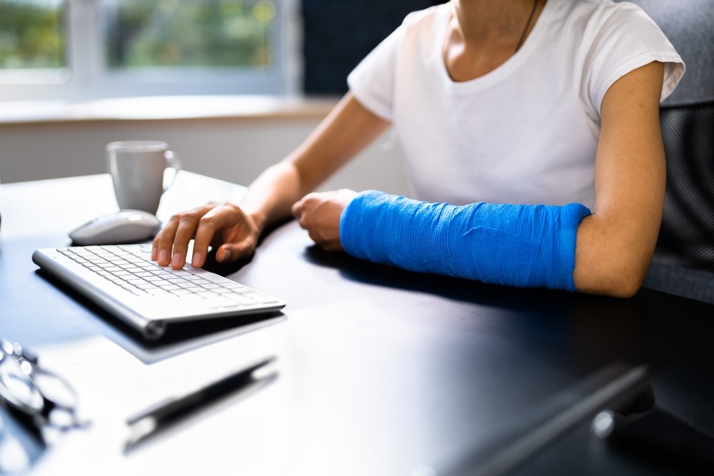 Worker with a broken arm in a cast typing at a desk after returning to work on a workers' comp claim