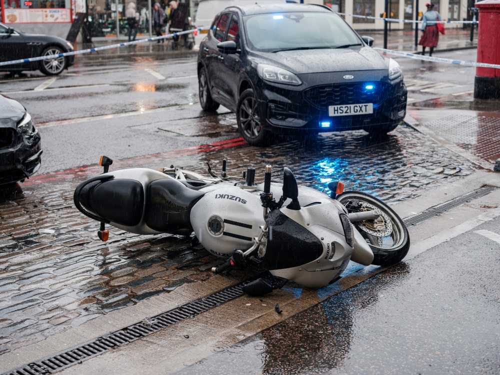 Motorcycle lying on wet pavement at a rainy crash scene with a damaged car and SUV nearby