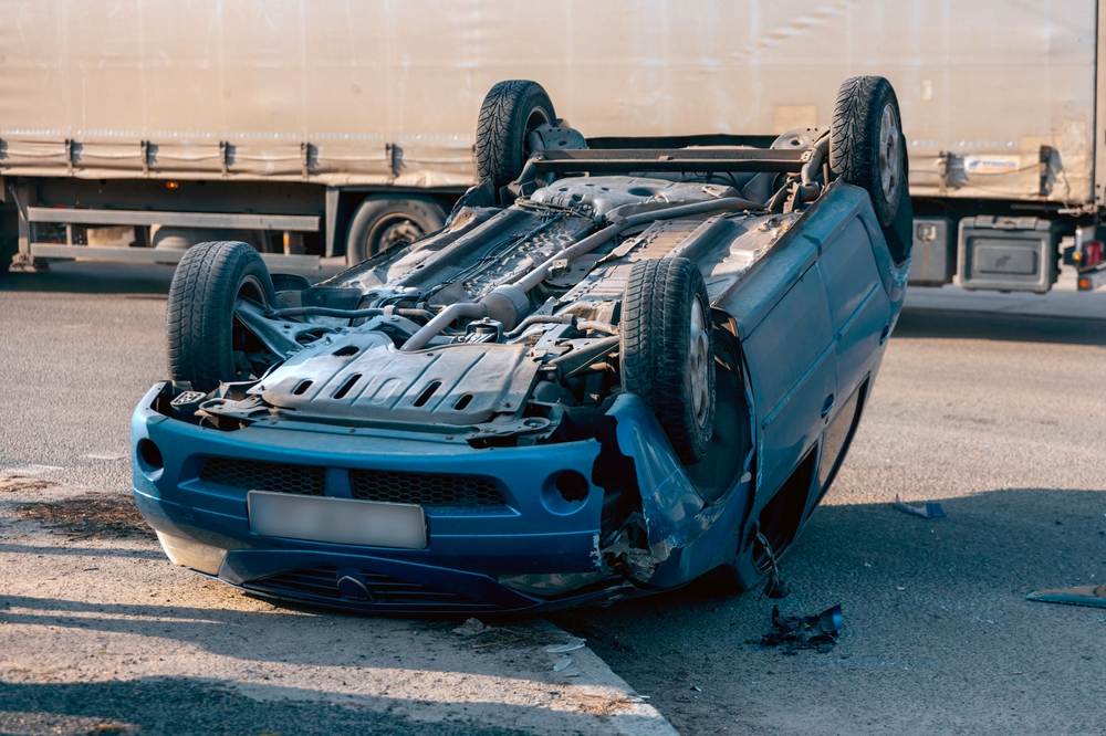 Overturned car with front-end damage on the road after a serious traffic accident near a truck