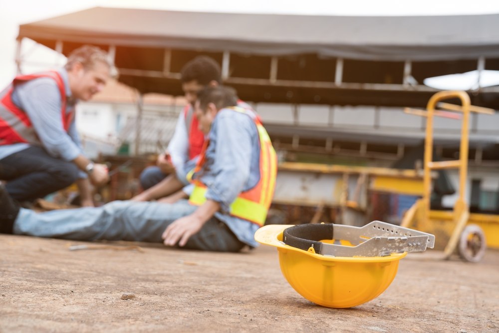 Yellow hard hat on the ground with coworkers tending to an injured worker in the background