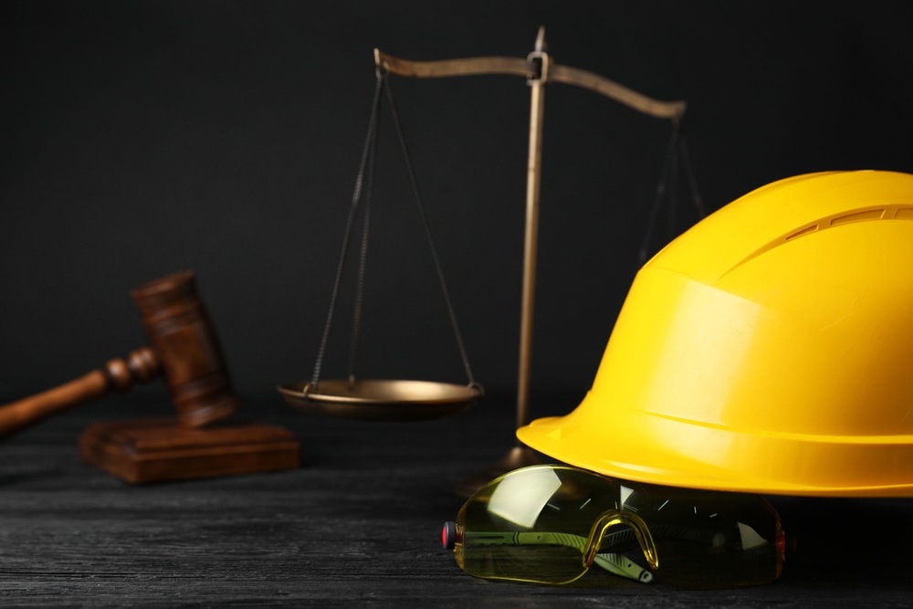 Yellow hard hat and safety glasses beside scales of justice and a gavel, representing a Philadelphia industrial accident case