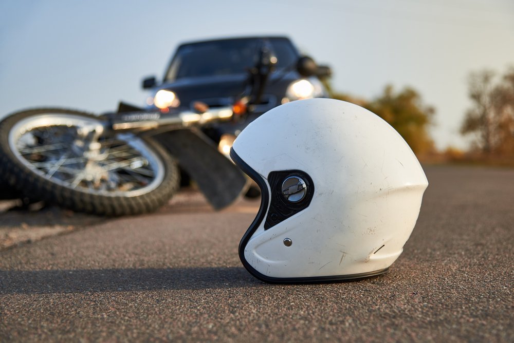 White motorcycle helmet resting on the road in front of a fallen motorcycle and a car with its headlights on