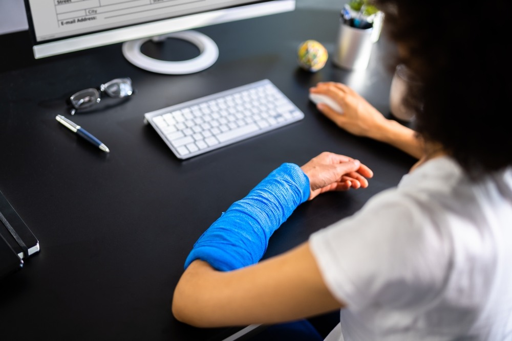 Office worker with her forearm in a blue cast using a computer mouse at her desk