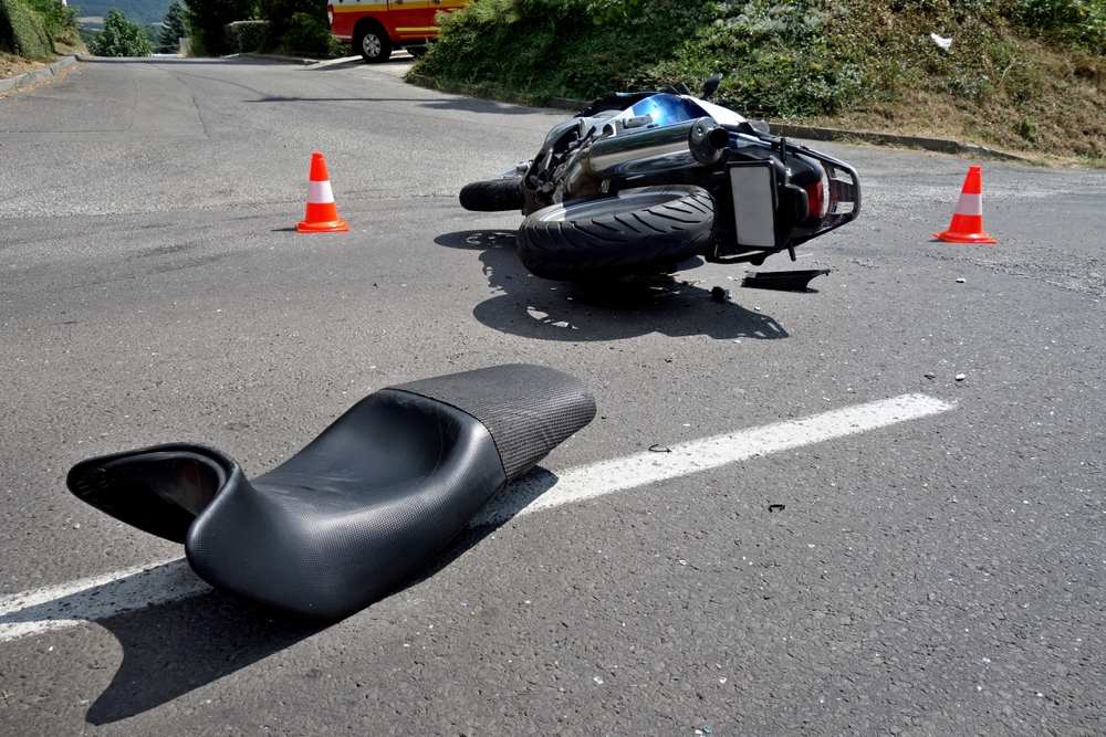 Motorcycle lying on its side after a crash, with its seat thrown across the lane and traffic cones set out around the scene