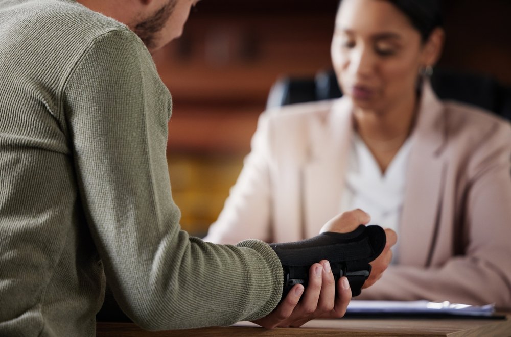 Injured man wearing a wrist brace sitting across a desk from a lawyer during a consultation